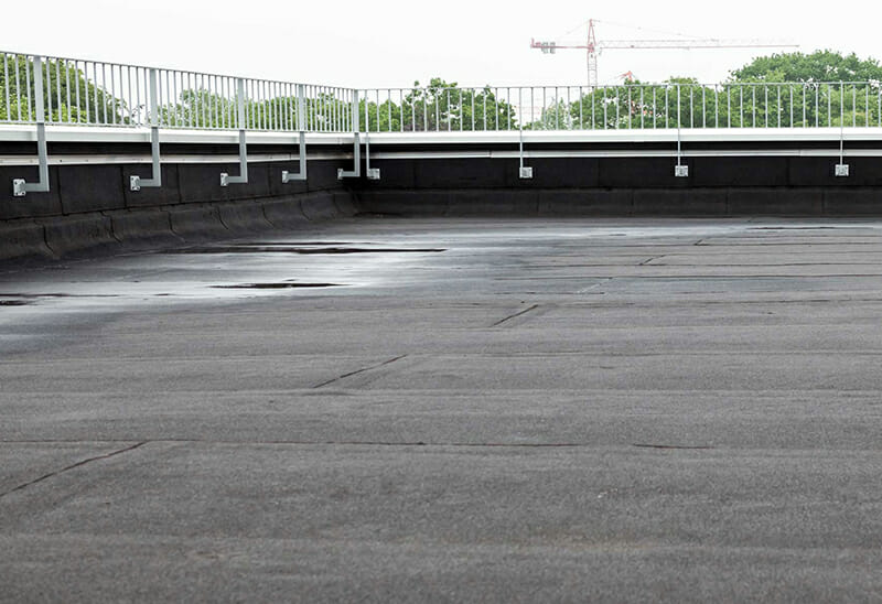 Flat commercial roof with black rubber roofing and safety railing along the edges image