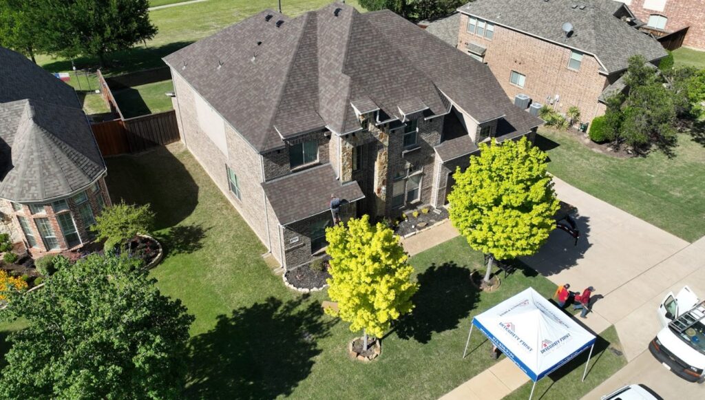 Aerial view of brick house with dark shingle roof and "Integrity First" tent on driveway.