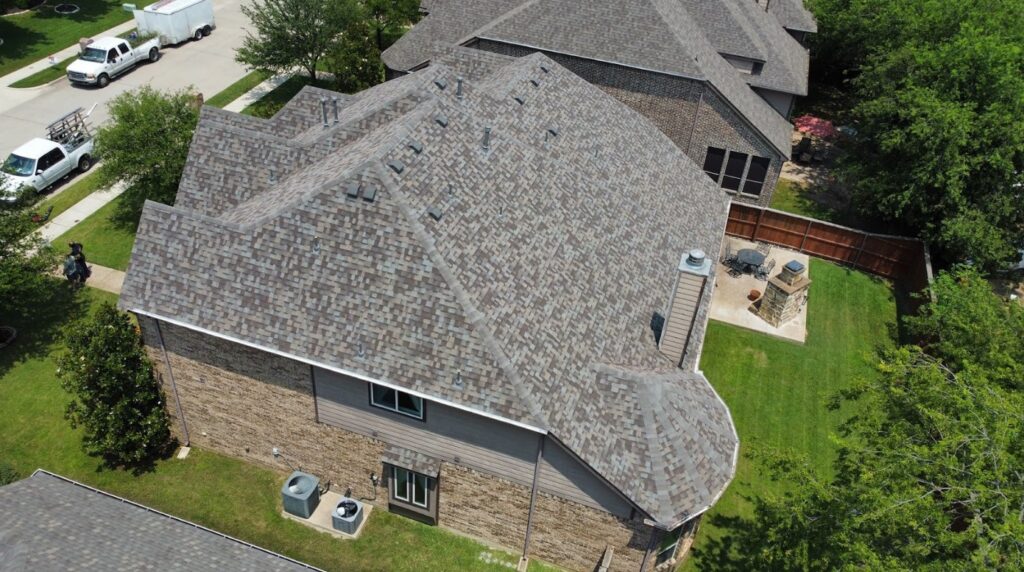 Aerial view of a suburban house with a complex, multi-gable roof covered in brown architectural shingles.