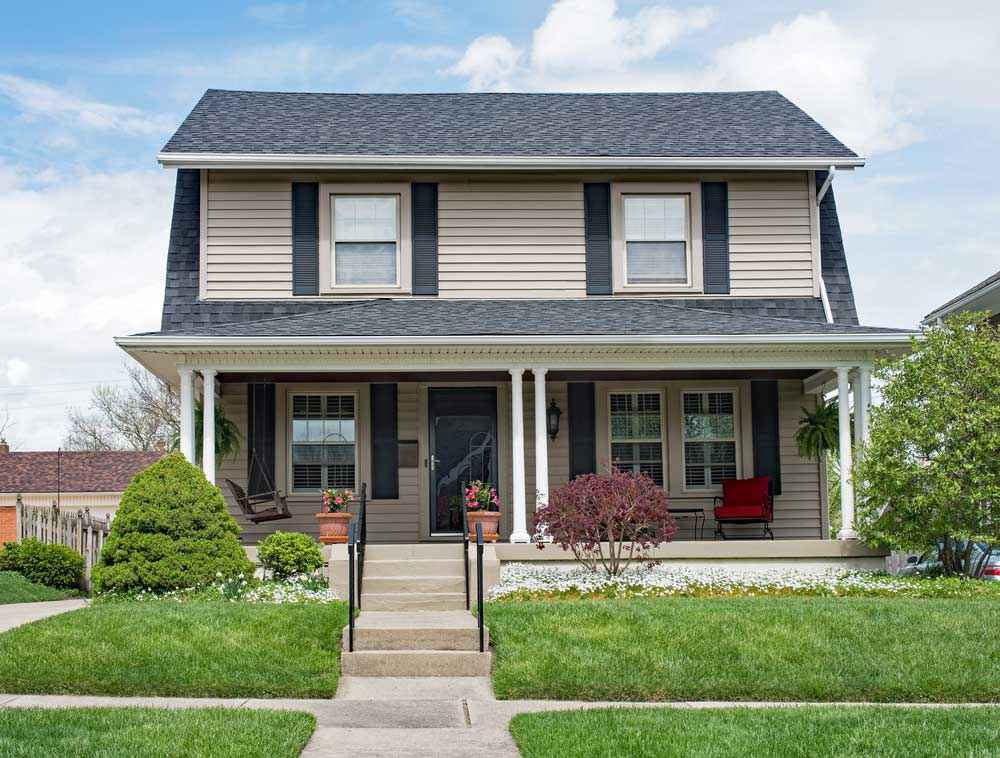 Charming two-story home with dark roof and inviting front porch.