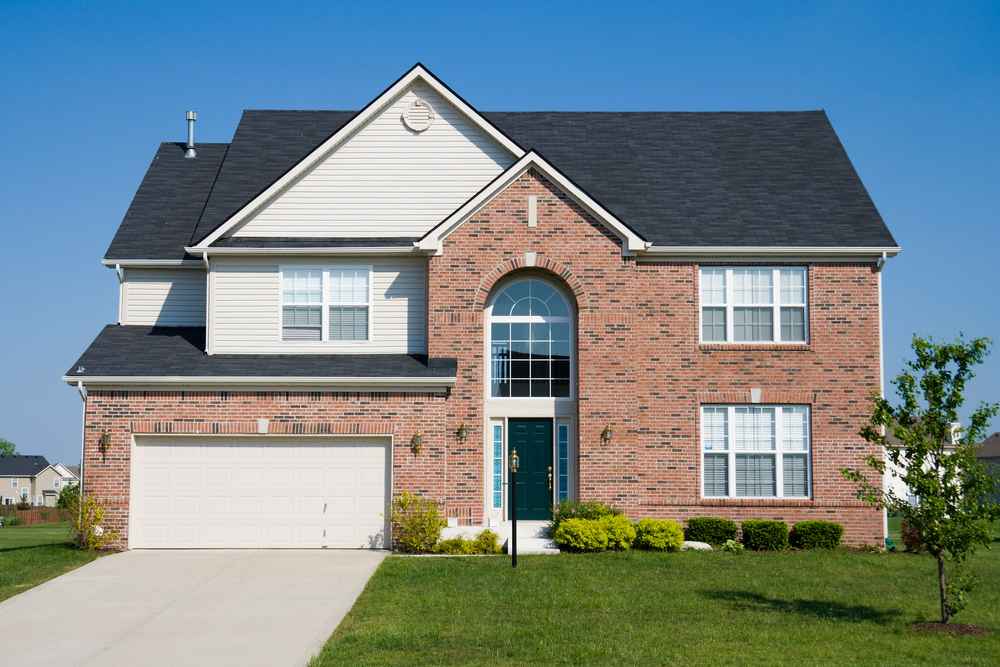 Two-story suburban house with brick facade, black shingle roof, and attached garage.